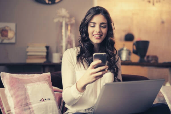 23-feature-woman-sitting-on-sofa-while-looking-at-phone-with-laptop-on-lap