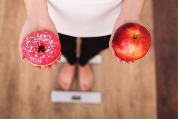diet woman measuring body weight holding apple and donut