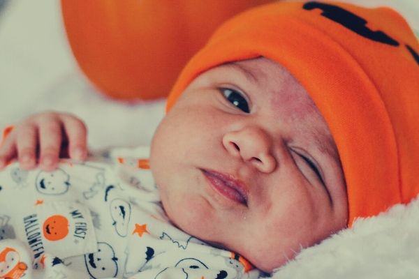 baby-wearing-orange-knitted-cap-photo-lying-near-pumpkin