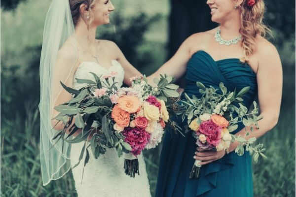 bride-bridesmaid-smiling-each-other-holding-bouquet-grass