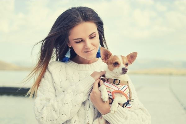 cute-woman-in-white-sweater-carrying-cute-dog-outside-sky-clouds
