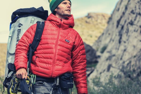 man hiking looking somewhere holding his shoes backpack red jacket