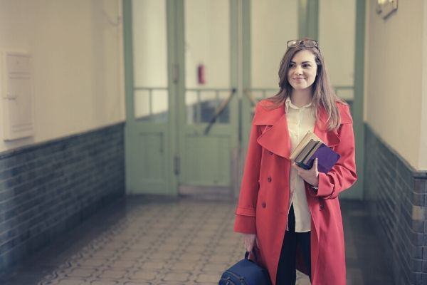 smart female student with books and backpack in university hallway pink blazer
