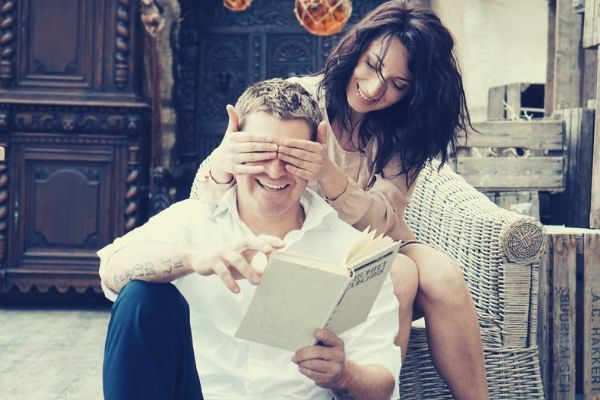 feature-woman-sitting-sofa-covering-mans-eyes-holding-book