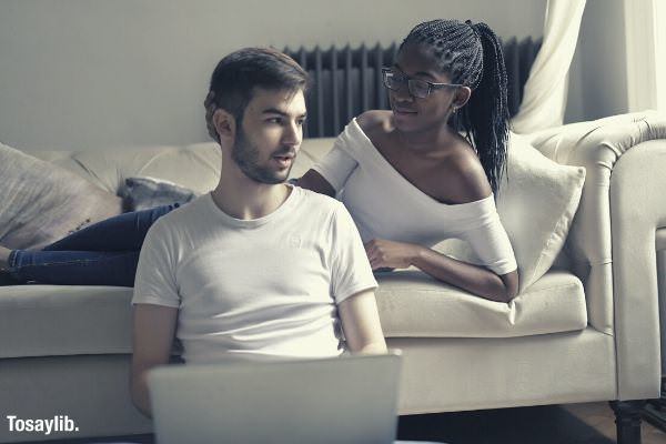 02 feature couple wearing white tops girl lying sofa man sitting holding laptop